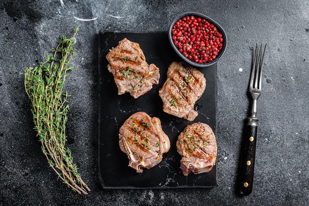 Grilled lamb loin chops steaks, cutlets on a marble board. Black background. Top view.