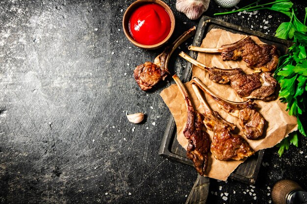 Grilled lamb rack on a cutting board with herbs and tomato sauce