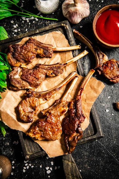 Grilled lamb rack on a cutting board with herbs and tomato sauce