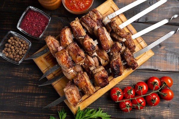 Grilled lamb ribs on cutting board on skewer with spices and sauce. Top view on dark wooden table