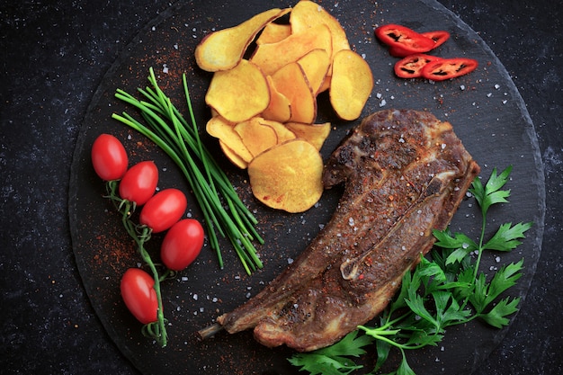 Grilled  lamb steak served with chips and vegetables on the cutting stone board.