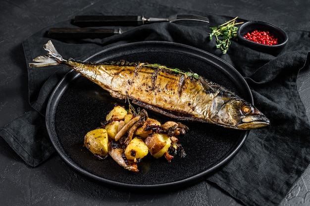 Grilled mackerel with baked potatoes and mushrooms. Black background. Top view