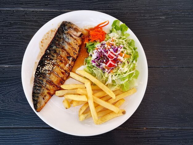 Grilled mackerel with salad and french fries on wooden background