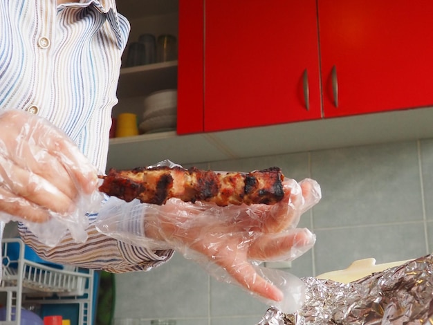 レストランからの使い捨て包装とアルミホイルに入った焼き肉 レストランやカフェからの宅配 使い捨て手袋をはめた女性の手が棒に肉を保持