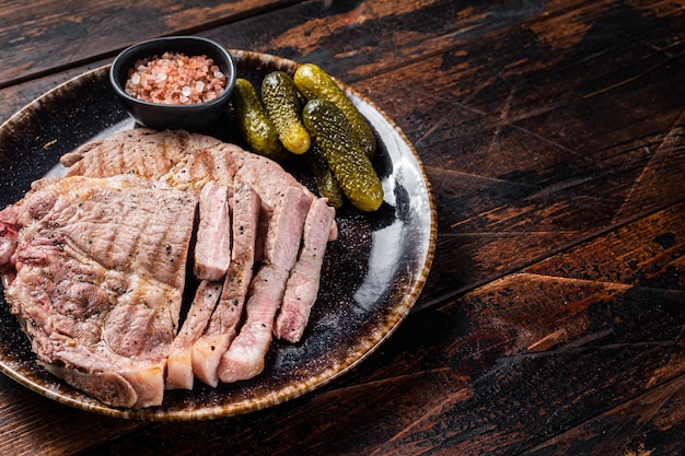 Grilled meat Pork steaks from neck fillet meat in plate with pickled cucumbers Wooden background Top view Copy space