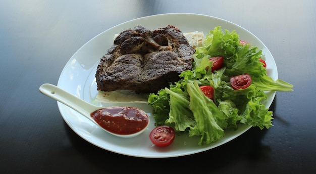 Grilled meat served with greens and pitta bread on white plate at the restaurant