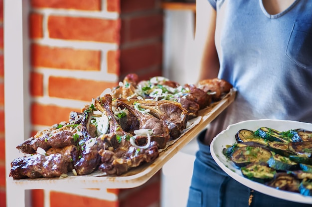 Grilled meat set on a wooden tray in the hands of a waiter