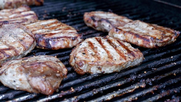 Grilled meat steak on stainless BBQ grill with flames on dark background Food and cuisine concept