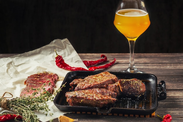 Мясо на гриле стейки на сковороде и стакан пива на темном деревянном фоне