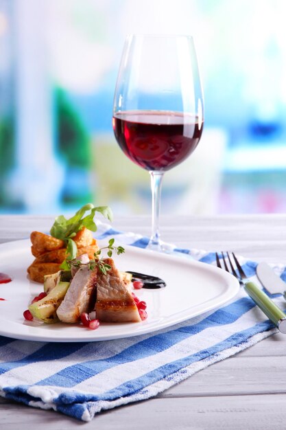 Grilled meat with fried potato marrow pieces and pomegranate seeds on plate on wooden table on bright background