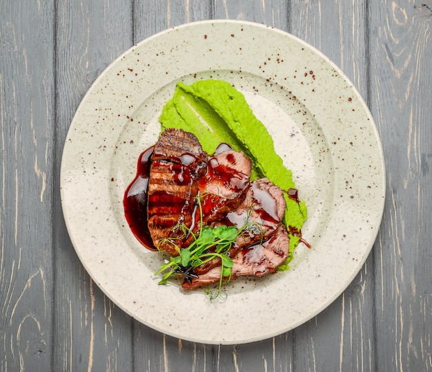 Foto carne alla griglia con salsa e verdure stufate su un tavolo di legno