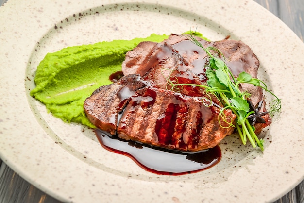 Grilled meat with sauce and stewed vegetables on a wooden table