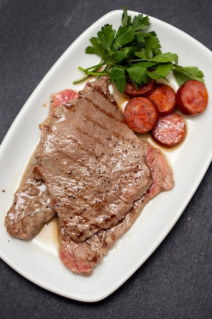 Foto carne arrostita con la salsiccia affumicata sul piatto bianco