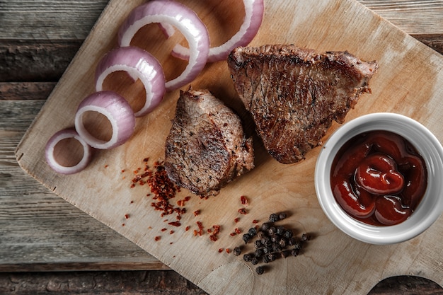 Grilled meat with spices and tomato sauce on a worn wooden background