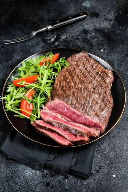 Grilled medium rare flank beef steak with salad in a plate Black background Top view
