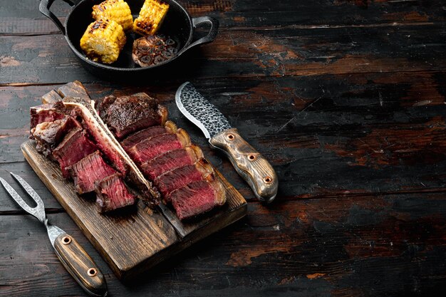 Grilled medium rare t bone or Porterhouse steak on wooden serving board on old dark wooden table background with copy space for text