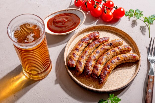 Salsicce macinate di manzo e maiale alla griglia con salsa barbecue su un piatto e un bicchiere di birra sul tavolo, foto con luce solare e ombre di tendenza.