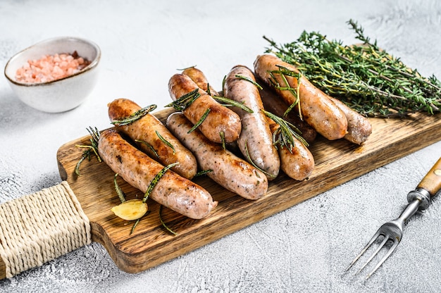 Grilled mix sausages with herbs on a cutting board. White background. Top view.