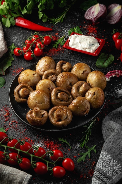 Photo grilled mushrooms in a dark plate on the table with spices vegetables herbs and onions