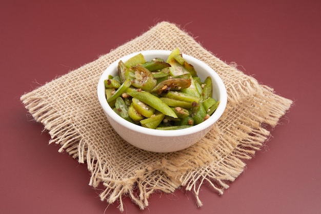 Grilled okra in a white bowl on a wooden table red background