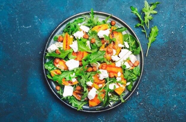 Grilled peach salad with feta cheese hazelnuts and arugula on blue background top view copy space