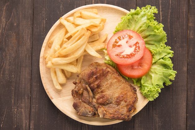 Bistecca e verdure arrostite di braciola di maiale con le patate fritte su legno