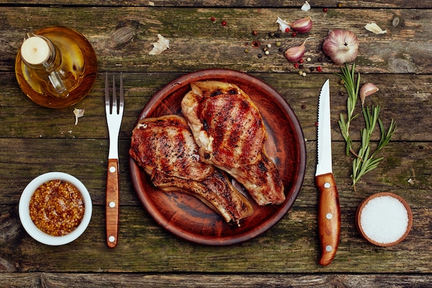 Grilled pork chops in a plate with fork and knife on an old wooden table.