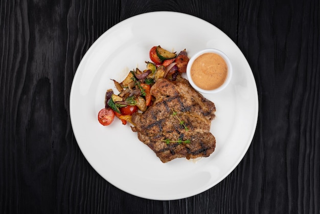 Grilled pork meat steak on white plate on black wooden background