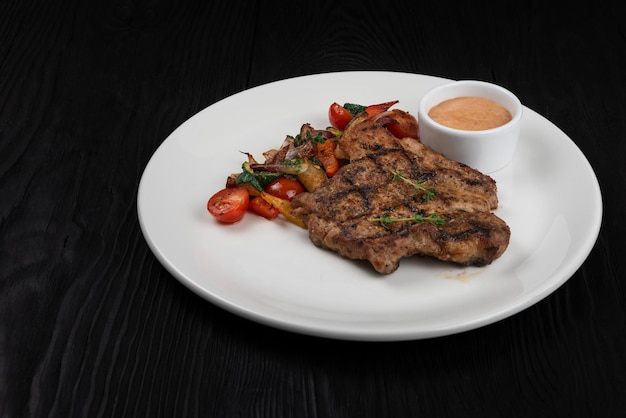 Foto bistecca di carne di maiale alla griglia su piatto bianco su fondo di legno nero