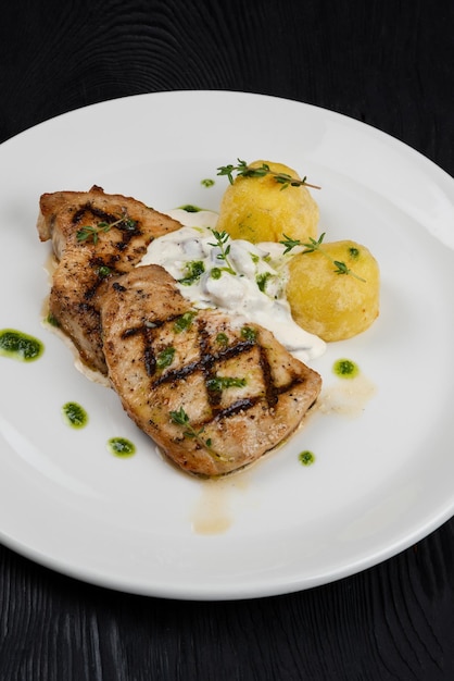 Grilled pork meat with mushroom sauce and potato on white plate on wooden black background