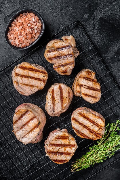 焼いた豚肉のメダリオンラックの上にあるテンダーローイン肉のステーキ黒い背景トップビュー