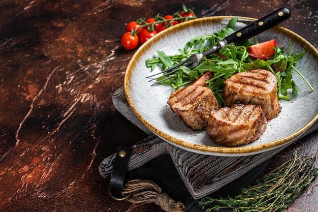 Grilled pork medallions steaks tenderloin fillet with salad in plate Dark background Top view Copy space