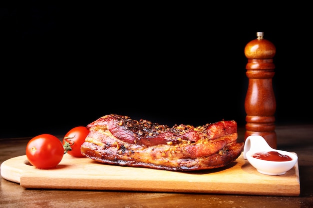 Costine di maiale alla griglia barbecue striploin bistecca con salsa e pomodori sul tagliere.