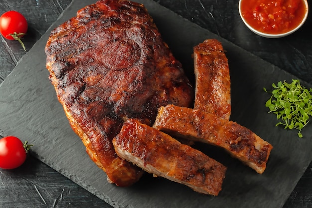 Grilled pork ribs, served on a graphite board with tomatoes