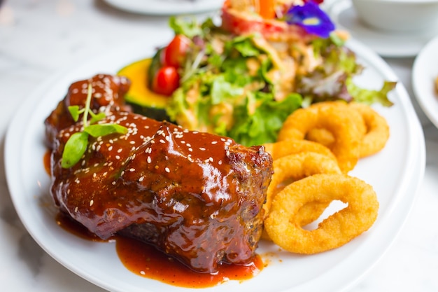 Grilled pork ribs with barbecue sauce and vegetables on a white plate