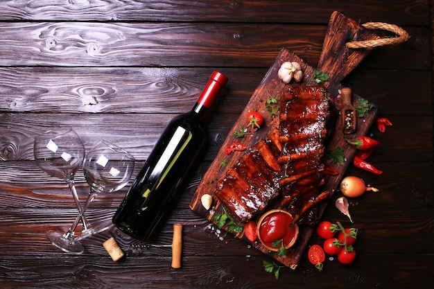 Grilled pork ribs with bottle of red wine spices and vegetables on wooden background