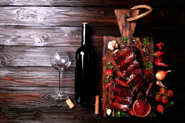 Grilled pork ribs with bottle of red wine spices and vegetables on wooden background