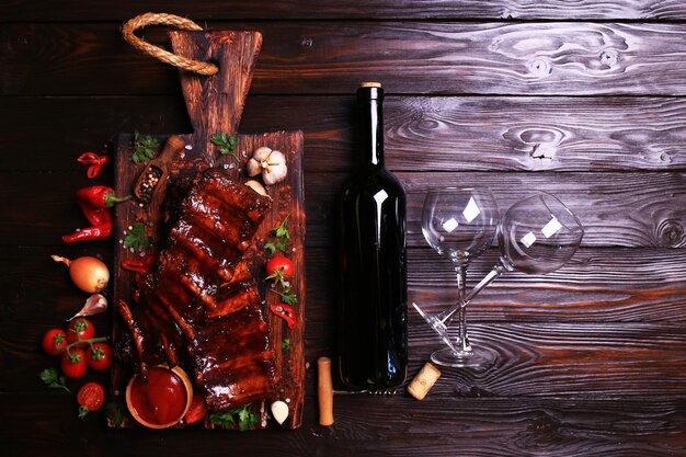 Grilled pork ribs with bottle of red wine spices and vegetables on wooden background