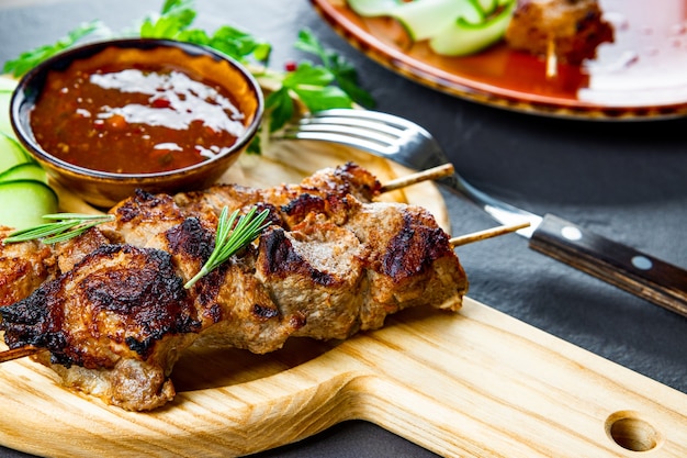 Grilled pork skewers with cucumber salad and barbecue sauce on the cutting board close up