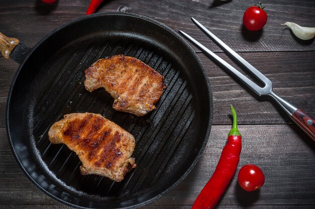 Grilled pork steak on pan, tomatoes and chili. Flat lay