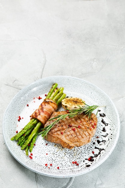 Grilled pork steak with asparagus and rosemary leaf on concrete table close up