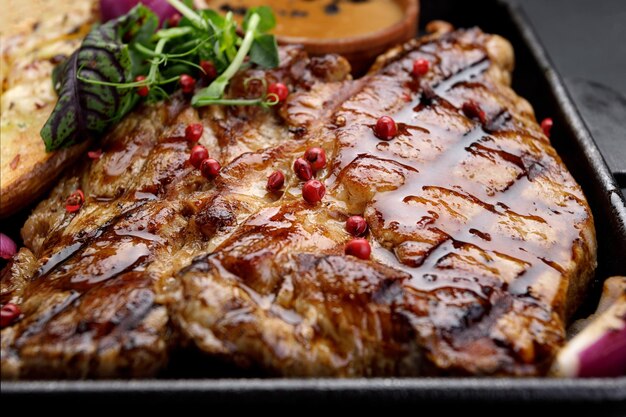 grilled pork steak with potatoes spices and sauce on a dark background in a frying pan