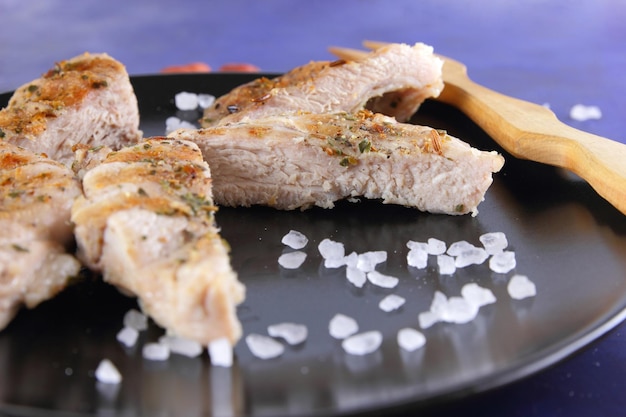 Grilled pork steak with spices on a blue background Pork steak with wooden fork and sea salt on a black plate Closeup