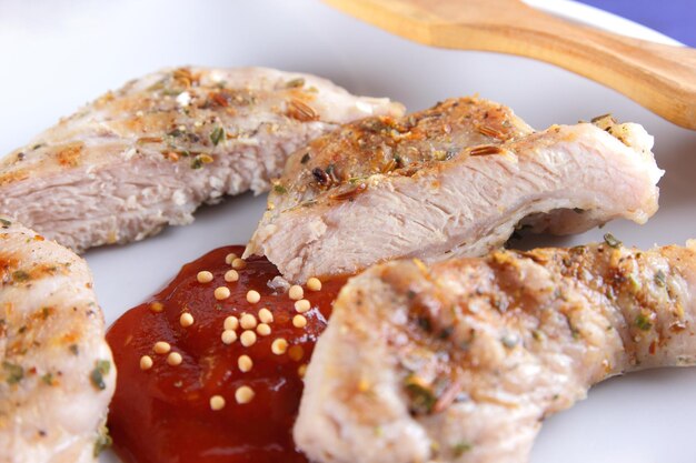 Grilled pork steak with spices on a table Pork steak with wooden fork and tomato sauce on a white plate Closeup