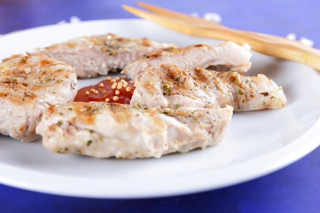 Grilled pork steak with spices on a table Pork steak with wooden fork and tomato sauce on a white plate Closeup