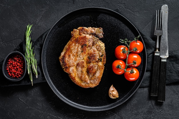 Grilled pork steak with tomatoes. Black background. Top view