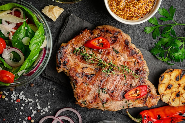 Bistecca di maiale alla griglia con verdure e insalata fresca su sfondo scuro