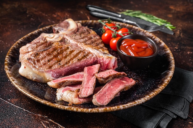 Grilled porterhouse beef meat Steak cooked t bone in a plate with tomato Dark background Top view