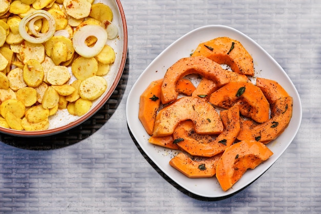 Grilled potatoes and orange butternut squash pieces on two plates - top down view