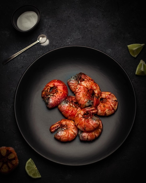 Grilled prawn shrimps with herbs, garlic and lime on the black plate searved on black stone background with sauceboat. top view